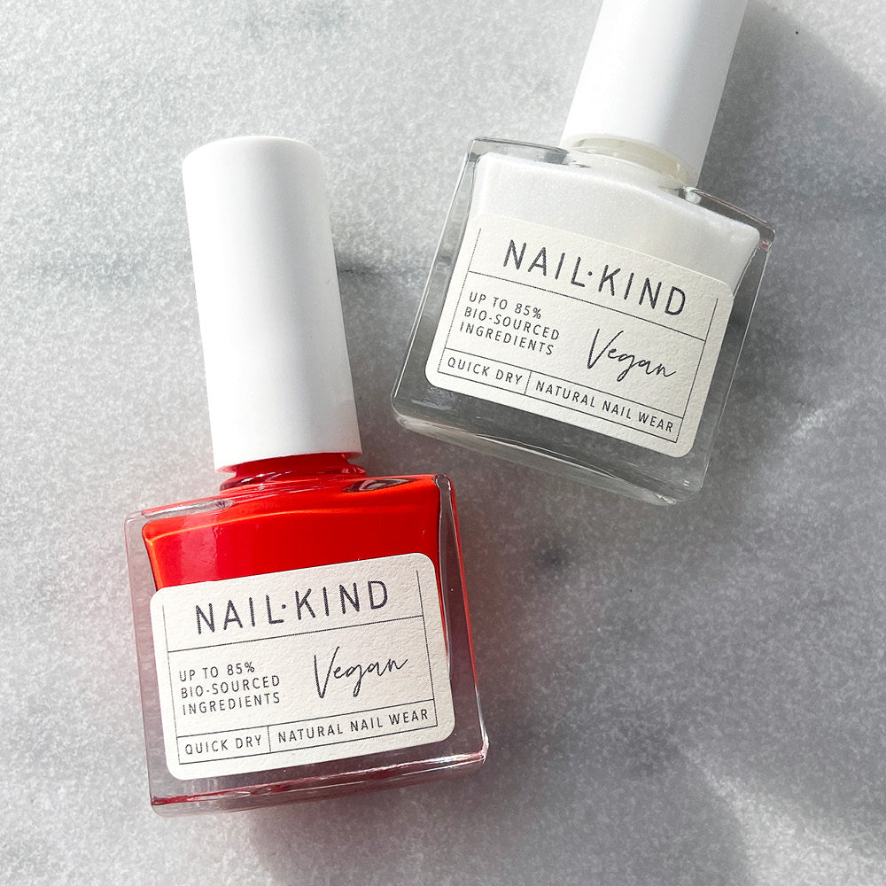 An orangey red nail polish and a sheer white nail polish lying next to each other on a marble background