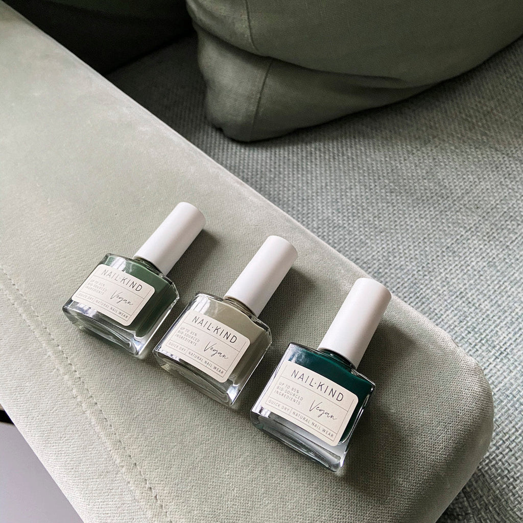 Three green nail polishes, lying down on the arm of a light green sofa