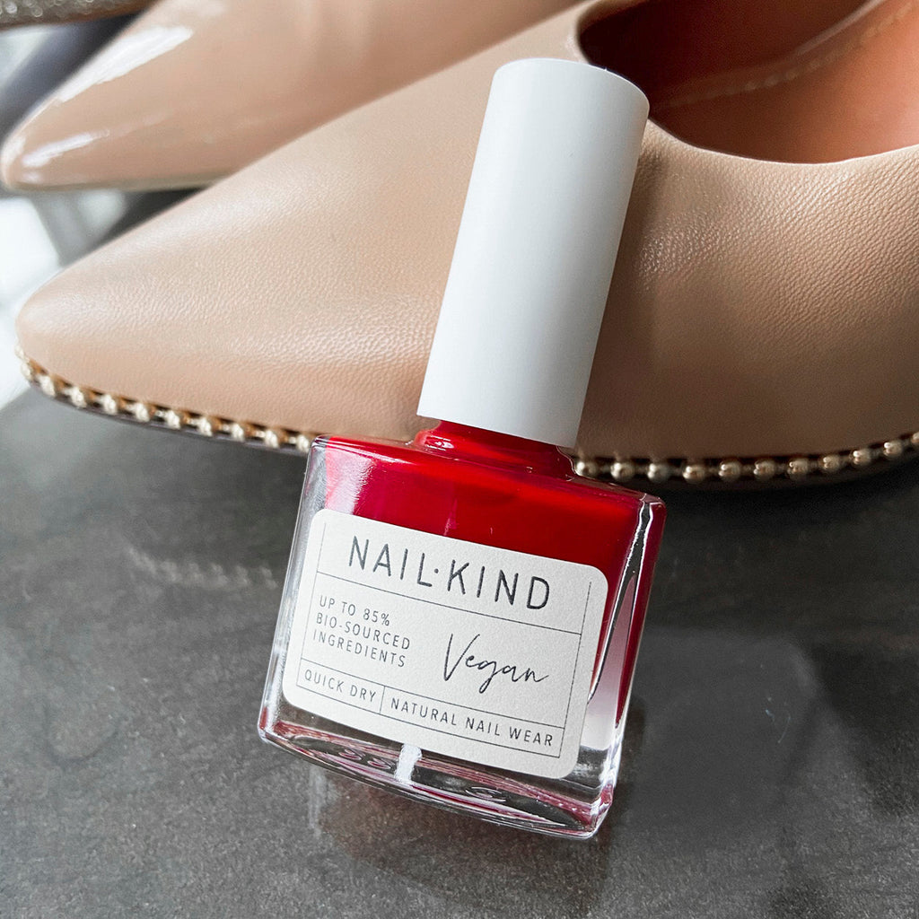 Bright red nail lacquer leaning on a beige women's high heel shoe