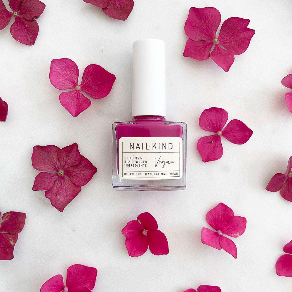 A medium pink nail varnish lying on a white background with medium pink flowers all around it